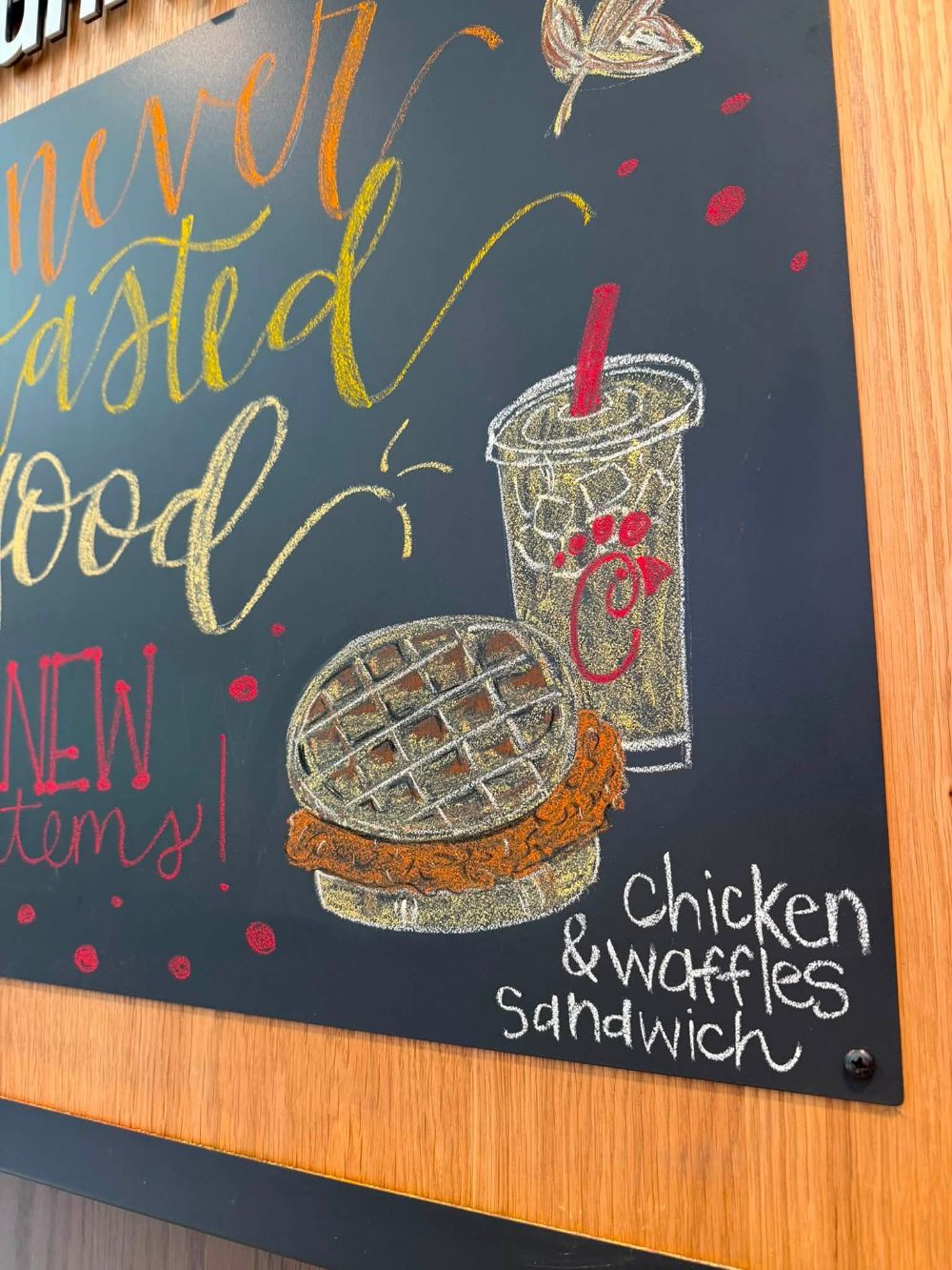 Chalkboard art detail: a chicken and waffles sandwich and iced drink drawn in chalk beside brush lettering reading new items