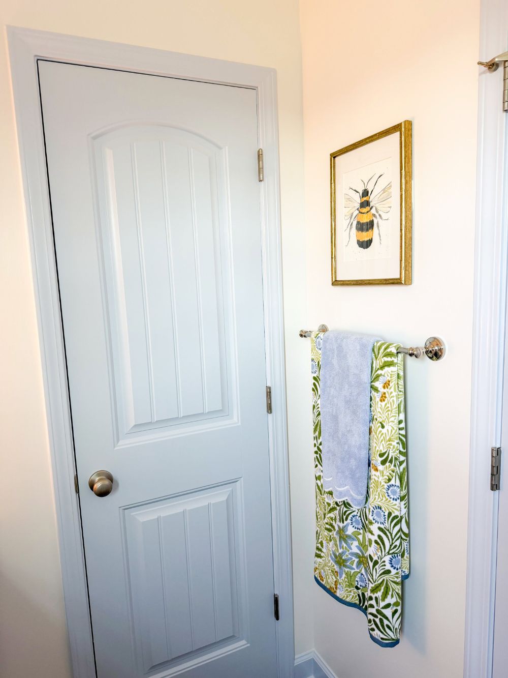 Bumblebee watercolor by Bailey Powers in a gold bamboo frame, hung above a towel bar with a green and blue floral towel