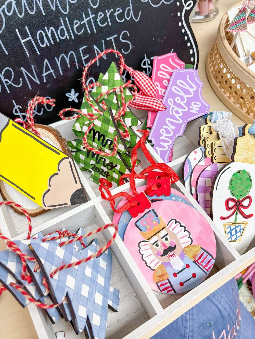 Hand painted and hand lettered wooden Christmas ornaments: gingham trees lettered Mr. and Mrs. 2024, a pink nutcracker, a Wendell NC state ornament, a topiary and a pencil