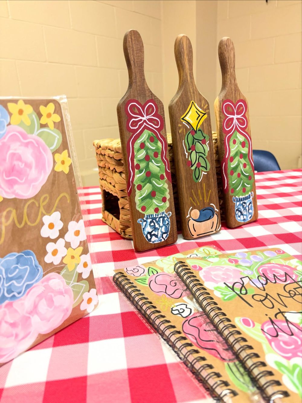 Hand painted wooden paddles with Christmas topiaries in blue and white chinoiserie pots and red bows, beside floral painted notebooks